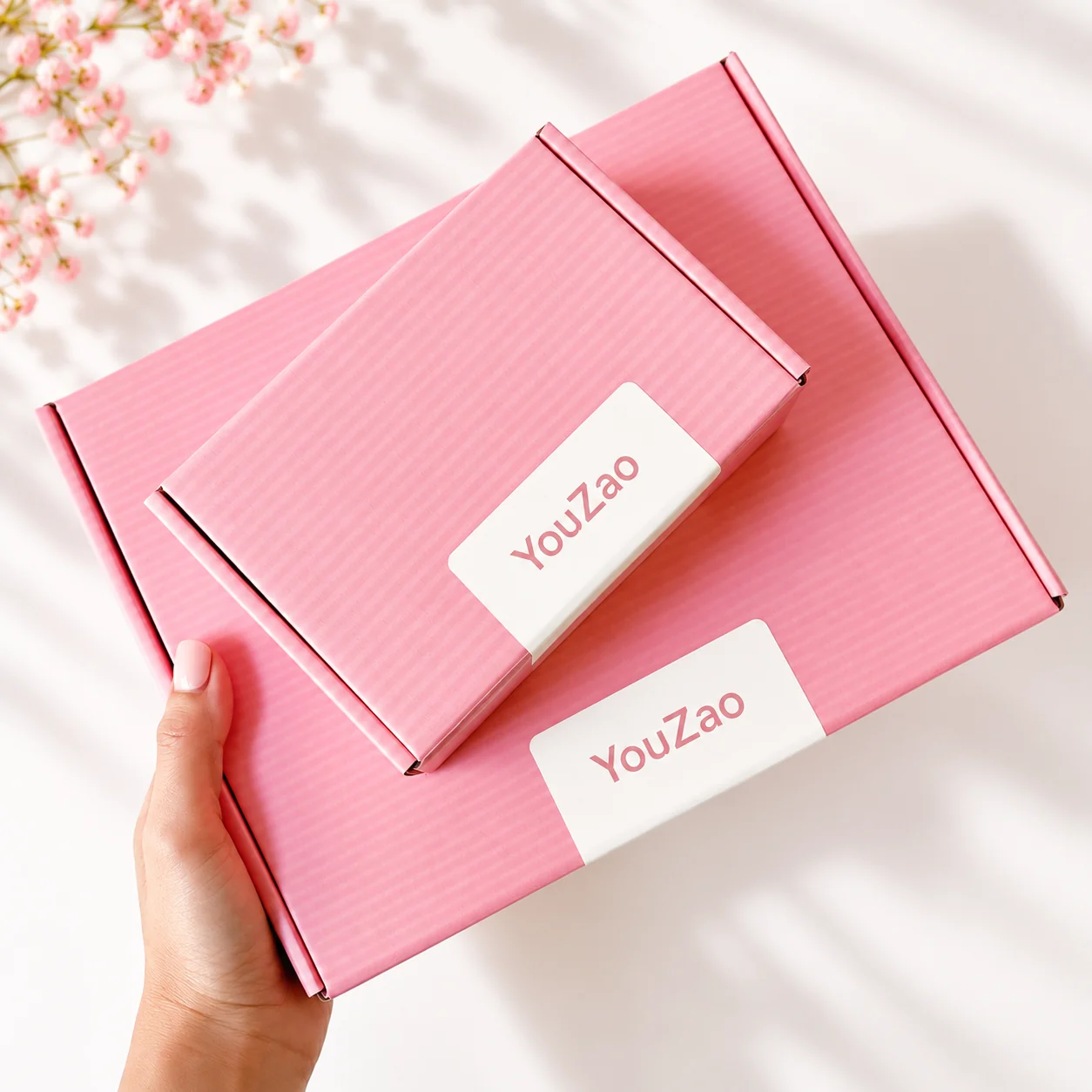 Handheld pink corrugated clothing mailer boxes showing lid and branding detail