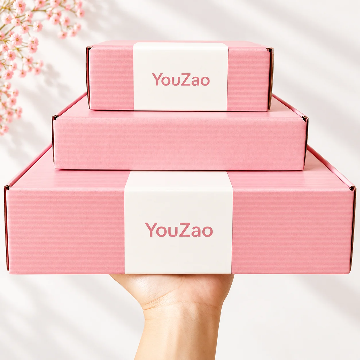Three pink clothing mailer boxes stacked on a hand