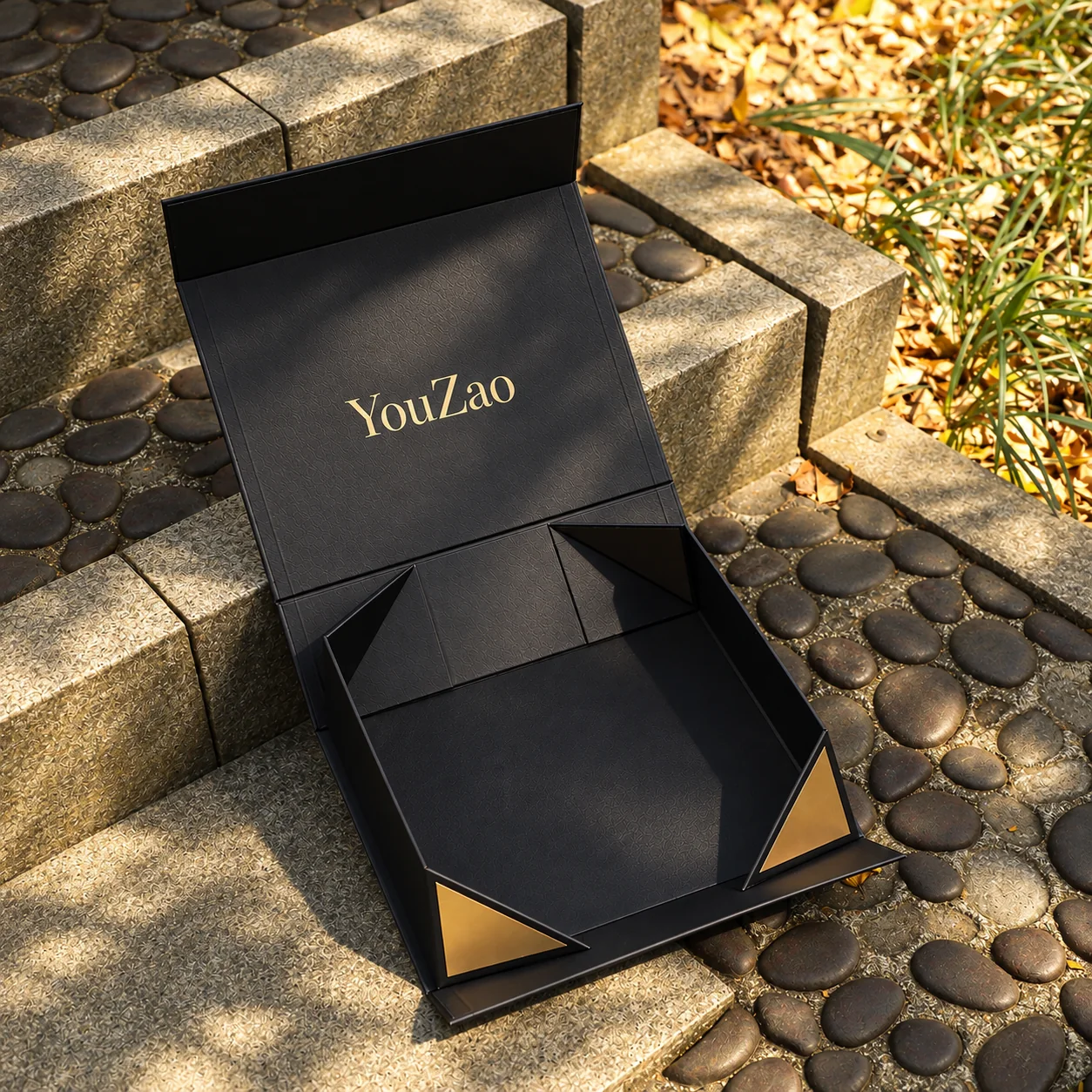 Open black gift box with gold corner accents on a stone surface