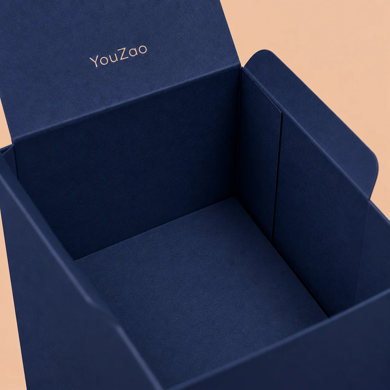 Open navy paperboard packaging box showing folded side flaps and an unfilled cavity